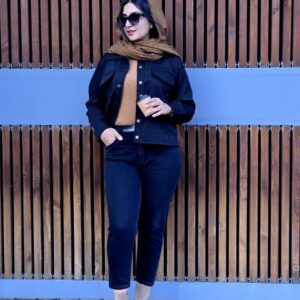 زنی با کت پاییزه سرمهای، شلوار مشکی و بوت کرم رنگ، با شالی قهوهای در فضایی مدرن و دیواری با طراحی چوبی دیده میشود.