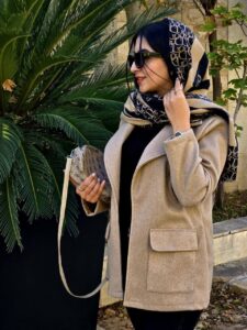 زنی با کت فوتر کرمی، شلوار مشکی و بوت کرمرنگ در فضایی کلاسیک ایستاده است؛ کت با طراحی مینیمال و پارچه گرم و مناسب فصل پاییز و زمستان.