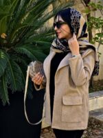 زنی با کت فوتر کرم، شلوار مشکی و بوت کرمرنگ در فضایی کلاسیک ایستاده است؛ کت با طراحی مینیمال و پارچه گرم و مناسب فصل پاییز و زمستان.