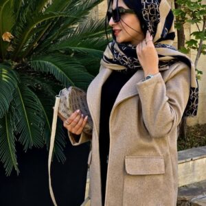 زنی با کت فوتر کرم، شلوار مشکی و بوت کرمرنگ در فضایی کلاسیک ایستاده است؛ کت با طراحی مینیمال و پارچه گرم و مناسب فصل پاییز و زمستان.